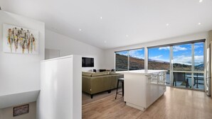 A modern kitchen with a large island, a dining area with a sofa, and a view of a mountainous landscape through large windows. - Top the Lake - Queenstown (Queenstown)