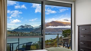A room with a large sliding glass door leading to a balcony with a scenic view of mountains and a lake. - Top the Lake - Queenstown (Queenstown)
