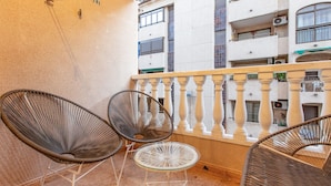 A balcony with wicker chairs and a glass table, overlooking a building with multiple balconies and windows. - Awesome apartment in Torrevieja (Torrevieja)