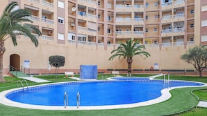 A swimming pool surrounded by a well-maintained lawn, with a multi-story building in the background. - Awesome apartment in Torrevieja (Torrevieja)