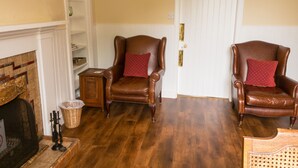 A room with two leather armchairs, a fireplace, wooden flooring, and a white door.