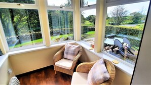 A corner room with wicker chairs, a view of a forest, and a table outside.