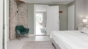 Un dormitorio con pared de ladrillo, una silla verde, una cama blanca y una puerta que da a un balcón.