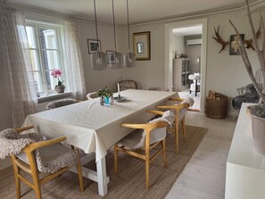 Ruokailuhuone, jossa on pitkä pöytä, tuoleja, maljakko kukkineen ja seinään kiinnitetty valaisin.