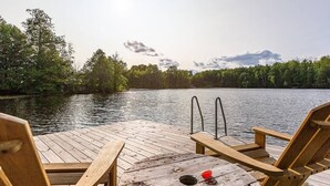 Un muelle de madera con sillas que da a un lago tranquilo, rodeado de árboles.