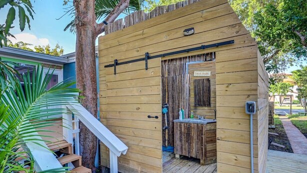Un baño exterior de madera con ducha, lavamanos e inodoro.