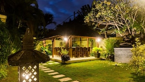 A well-lit outdoor seating area with a covered structure, surrounded by a manicured lawn and tropical plants. - Luxury Private Villa in Heart of Seminyak (Seminyak)