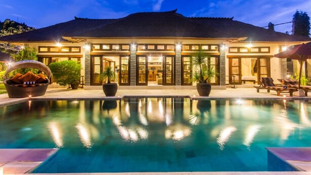 A large, well-lit building with a swimming pool in front, surrounded by potted plants and outdoor seating. - Luxury Private Villa in Heart of Seminyak (Seminyak)