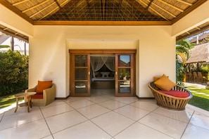 A room with a tiled floor, a wooden ceiling, and a glass door leading to a bed. There are two wicker chairs with cushions. - Luxury Private Villa in Heart of Seminyak (Seminyak)