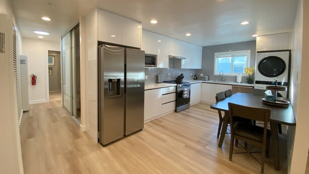 A modern kitchen with a stainless steel refrigerator, a built-in oven, and a dining area with a table and chairs. - Elegant Beachside 2B1B Retreat • Newly Renovated • Free Parking • 15min SF/SFO (Pacifica)