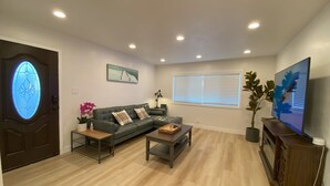A living room with a green sofa, a coffee table, a TV, and a window with blinds. - Elegant Beachside 2B1B Retreat • Newly Renovated • Free Parking • 15min SF/SFO (Pacifica)