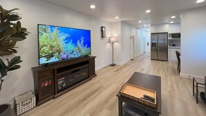 A modern living room with a flat-screen TV, wooden entertainment unit, and a chess table. - Elegant Beachside 2B1B Retreat • Newly Renovated • Free Parking • 15min SF/SFO (Pacifica)