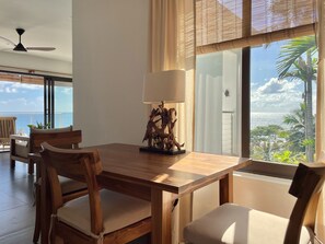 A wooden dining table with chairs, a decorative lamp, and a view of the ocean through large windows.