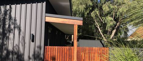 A modern building with a grey facade, a wooden deck, and a fence.
