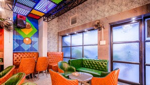 Un espace détente avec un canapé vert, des fauteuils orange et un mur orné de motifs.