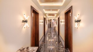 Un couloir d’hôtel avec des portes en bois, un sol en marbre et des appliques murales modernes.