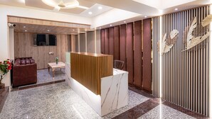 Un espace d’accueil avec un comptoir de réception en bois, un coin salon avec un canapé marron, une petite table et un mur décoratif agrémenté de panneaux verticaux.