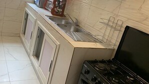 A compact kitchen with a gas stove, a sink, and cabinets. - Logement Entier : Appartement 3 Pièce (Cotonou)