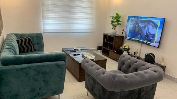 A living room with two sofas, a coffee table, and a television mounted on the wall. - Logement Entier : Appartement 3 Pièce (Cotonou)