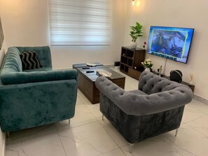 A living room with two sofas, a coffee table, and a television mounted on the wall. - Logement Entier : Appartement 3 Pièce (Cotonou)