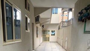 A corridor with tiled flooring, a central door, and windows on both sides. - Logement Entier : Appartement 3 Pièce (Cotonou)