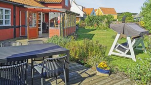 A patio with a table and chairs, a barbecue grill, and a garden with a lawn and plants.