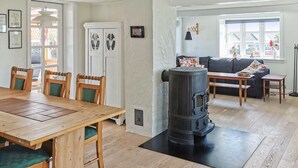 A cozy living room with a wooden dining table, chairs, a sofa, and a large black wood-burning stove.