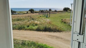 A view of a beach with a dirt path, a swing set, and a small building in the distance.