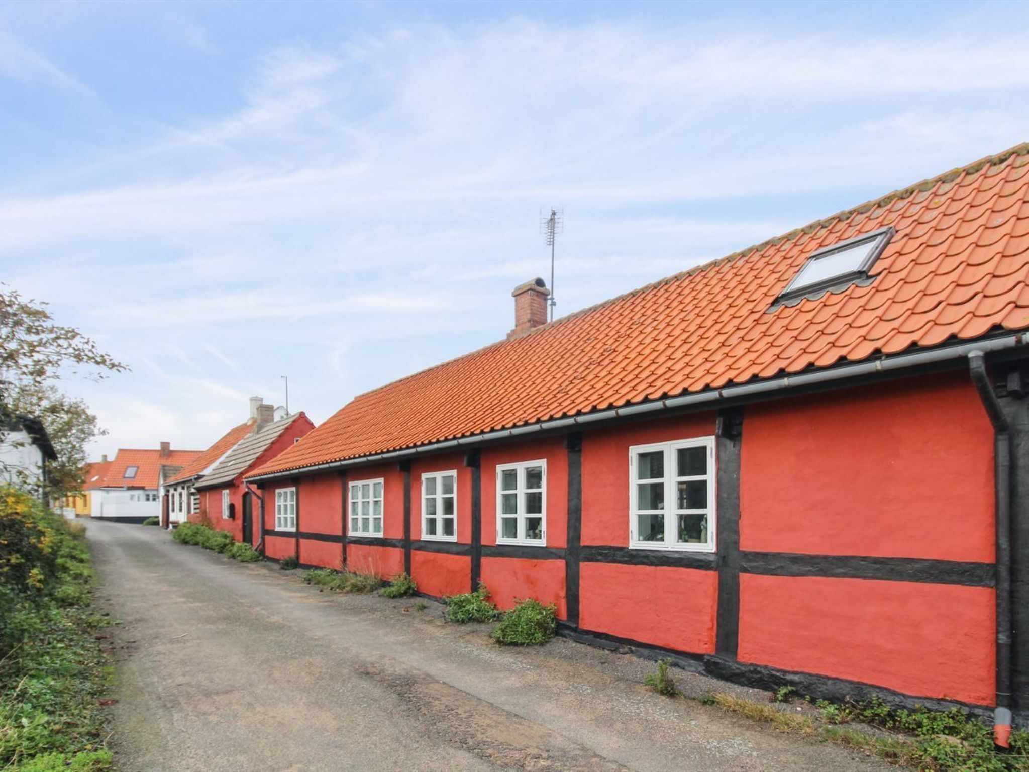 A row of red houses with black trim and white windows, a gravel road, and a clear sky.
