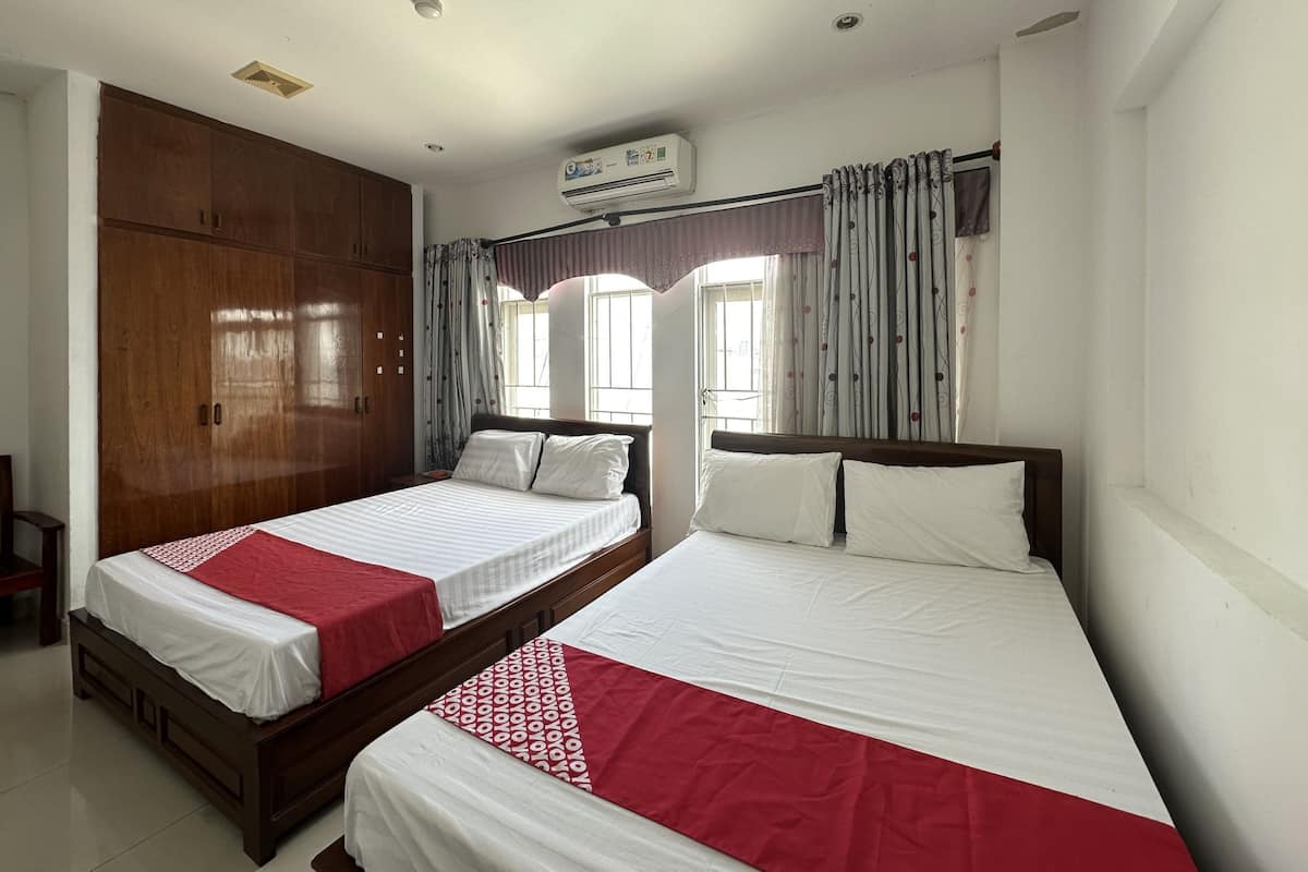 A hotel room with two beds, a wardrobe, an air conditioning unit, and a window with curtains.