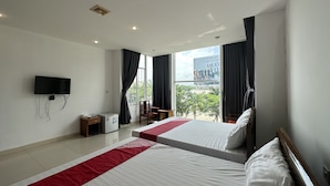 Habitación de hotel con dos camas, un televisor montado en la pared, una mesita pequeña y una ventana con cortinas.