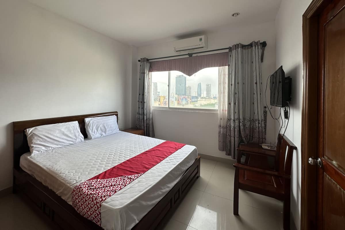 A bedroom with a bed, a TV, and a window with curtains.