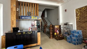 Zona de recepción de un hotel con un mostrador de madera, un reloj y una escalera que sube al piso superior.
