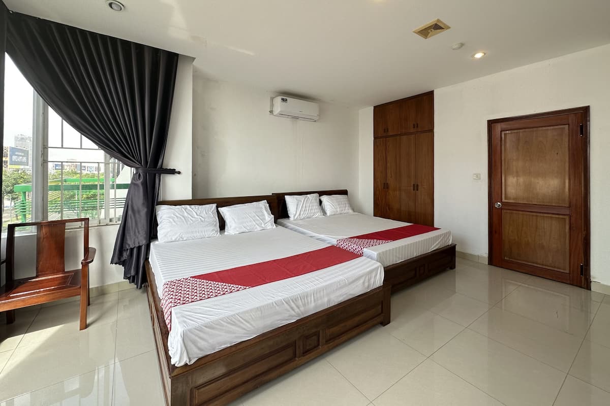 A double bed with white and red bedding, a wooden wardrobe, a wooden chair, and a window with curtains.