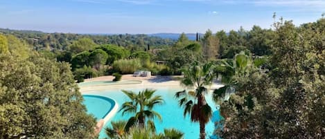 A pool surrounded by lush greenery and trees, with a clear blue sky above.