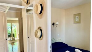 A hotel room with a bed, two rolled towels, a wall-mounted lamp, and a door leading to a balcony.