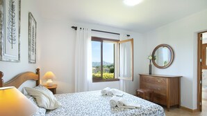 A bedroom with a bed, bedside lamps, a dresser, a mirror, and a window with curtains. - VILLA GABRIEL - RUSTIC STAY (Alcúdia)
