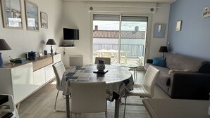 Un comedor con una mesa redonda, sillas, un televisor y un balcón con vistas.
