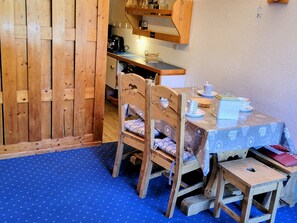 A wooden dining table with chairs, a blue patterned tablecloth, and a small wooden stool.