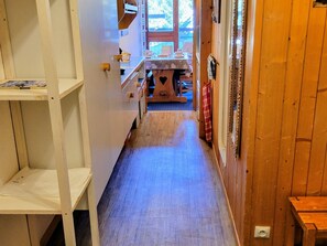 A narrow hallway with wooden flooring leading to a dining area with a table and chairs.