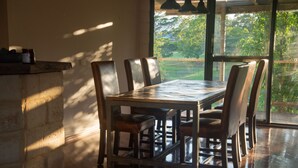 Un comedor con una mesa y sillas de madera, una pared de piedra y vistas a la vegetación exterior.