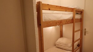 A bunk bed with white bedding in a room with a wooden door and white walls. - Cozy studio 4 pax · Balcony · Wifi · Pets allowed (Tignes)