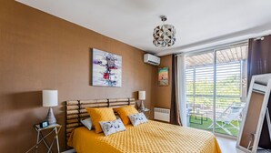 A bedroom with a large bed, two bedside lamps, a ceiling light, a window with a view of greenery, and a wall-mounted air conditioner. - Biscarrosse beach, air-conditioned apartment with wifi, center, 4 pax (Biscarrosse Plage)