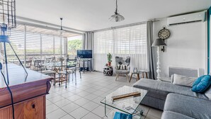 A spacious living room with a dining area, large windows, a ceiling fan, and a TV. - Biscarrosse beach, air-conditioned apartment with wifi, center, 4 pax (Biscarrosse Plage)