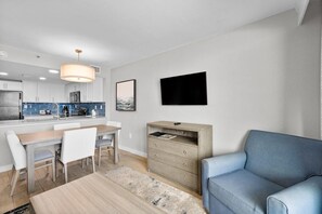 A modern kitchen with white cabinets, a blue backsplash, and a dining area with a wooden table and white chairs. - Seaside Splendor: Oceanfront Deluxe 2 Bedroom Condo (Myrtle Beach)