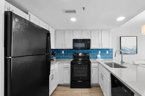 A modern kitchen with white cabinets, a black refrigerator, a microwave, an oven, and a dishwasher.