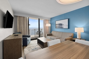 A hotel room with a balcony, a TV, a sofa, a dining table, and a lamp.