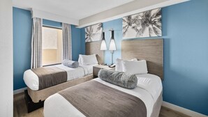 Ett hotellrum med två sängar, ett nattduksbord, en lampa och ett fönster med gardiner.