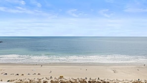 En strand med klar himmel, sandstrand och några få personer.