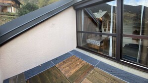 A modern building with a large window, wooden deck, and a view of a forested mountain area.